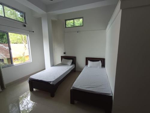 two beds in a room with two windows at Devagram Guest house in Dergaon