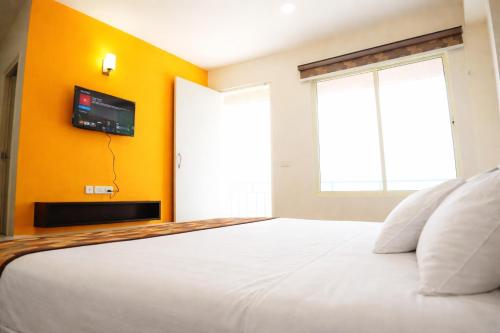 a bedroom with a white bed and a tv on a yellow wall at Mandola Stays in Girgaon
