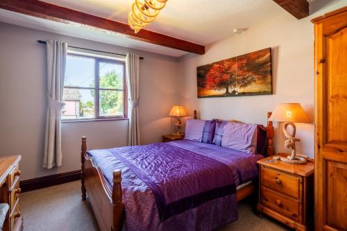 a bedroom with a purple bed and a window at Trenewydd Farm Holiday Cottages in Cardigan