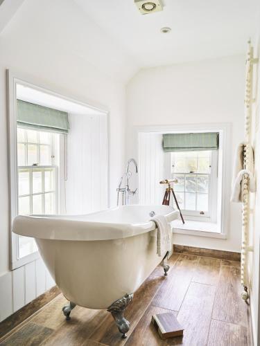 a white bath tub in a bathroom with two windows at Lugger Hotel ‘A Bespoke Hotel’ in Portloe