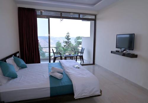 a bedroom with a bed with a television and a balcony at Hotel Sunrise, Panchgani in Panchgani