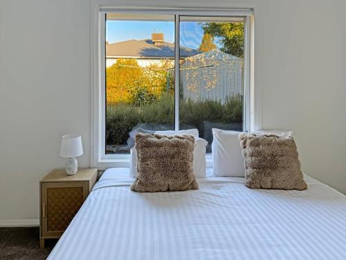a white bed with two pillows and a large window at St Pauls Home in North Wagga