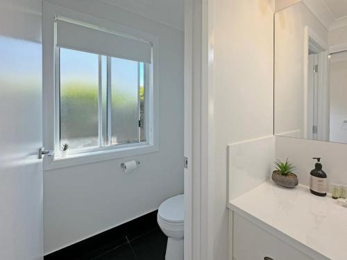 a white bathroom with a toilet and a window at Paradise Stay in North Wagga