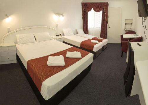 a hotel room with two beds and a desk at Calico Court Motel in Tweed Heads