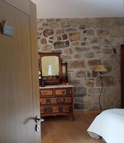a bedroom with a stone wall with a dresser and a mirror at Cantinho do Ribeiro in Lourosa da Trapa