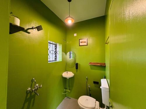 a green bathroom with a toilet and a sink at The Habitat By Locomo in Mandrem