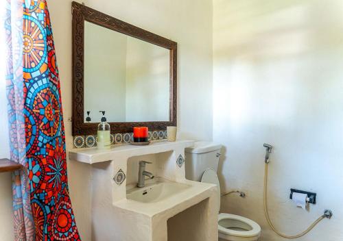 a bathroom with a sink and a mirror and a toilet at Ella's Swahili Villa - Restored 1840s Heritage Home in Bagamoyo