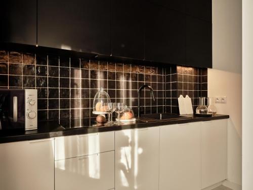 a kitchen with white cabinets and black tiles on the wall at Apartamenty Media Park in Warsaw