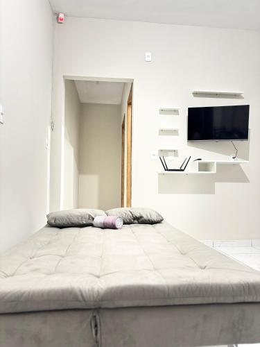 a large bed in a white room with a flat screen tv at Studio Confortável no Centro com Garagem in Araquari
