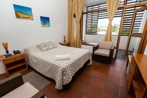 a bedroom with a bed and a chair and a window at Posada del Mar in Puerto Ayora