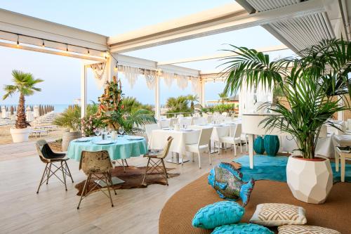a restaurant with tables and chairs and palm trees at Hotel Bellariva in Lido di Jesolo