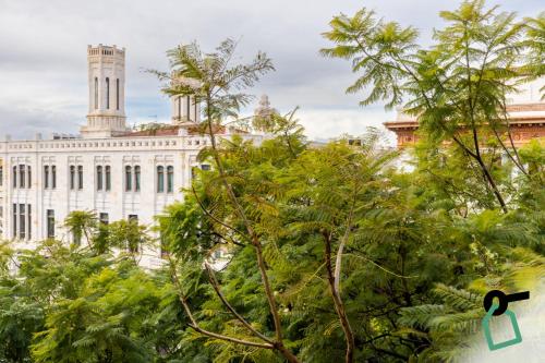 a large white building with a clock tower behind trees at Hotiday Cagliari Lungomare in Cagliari
