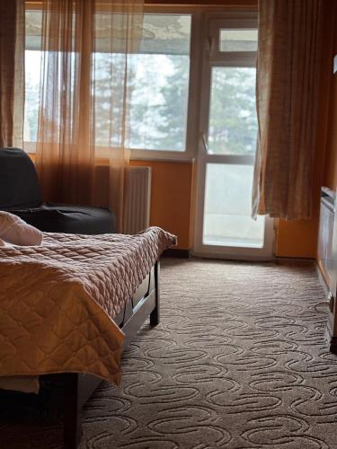 a bedroom with a bed and a chair and windows at Парк-хотел Родопи in Churen