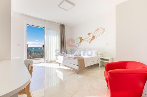 a white bedroom with a bed and a red chair at Residence Stella del Mare in Torre Pali