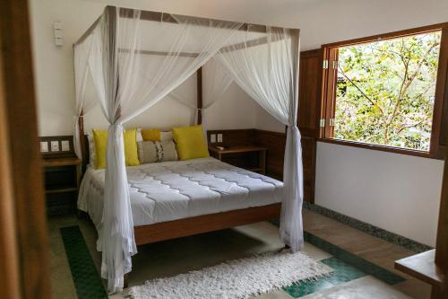 a bedroom with a canopy bed with a window at Pousada Vila do Beco in Arraial d'Ajuda