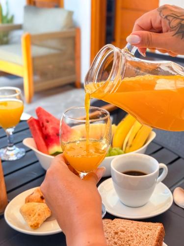 a person pouring orange juice into a glass on a table at Pousada Praia do Carioca Búzios in Búzios