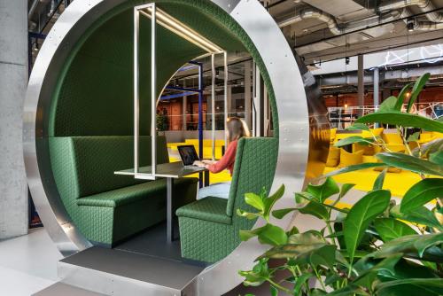 a woman sitting in a green chair with a laptop at The Social Hub Delft Extended Stay in Delft