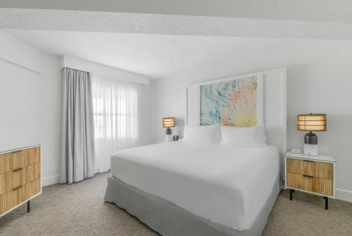 a white bedroom with a large bed and a window at Beach House Suites by the Don CeSar in St. Pete Beach