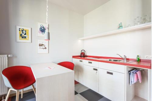 a kitchen with white cabinets and red chairs and a sink at Hotel & Restaurant Michaelis in Leipzig