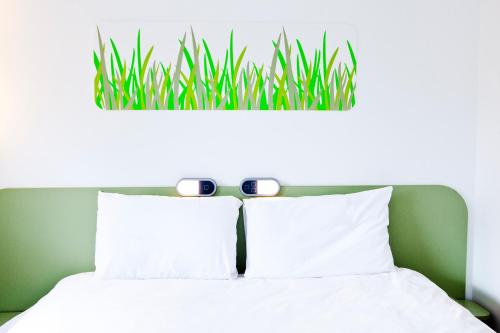 a bed with white pillows and a green head board at Ibis Budget Sarrebourg Buhl in Sarrebourg