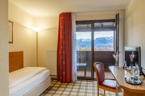 a hotel room with a bed and a desk and a window at Panoramahotel Kühbergalp in Gunzesried