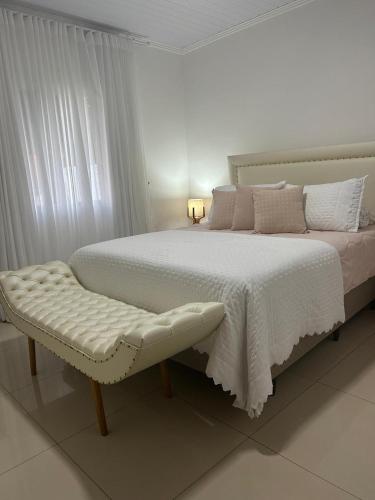 a white bedroom with a large bed and a bench at Casa de lazer e tranquilidade in Tramandaí
