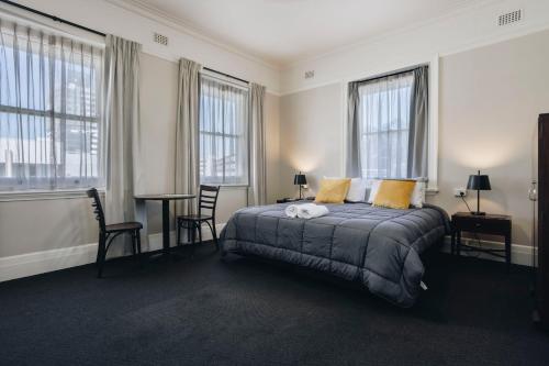 a bedroom with a bed with two chairs and windows at Hotel Gosford in Gosford