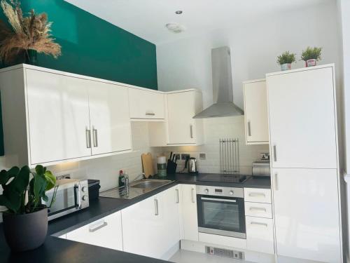 a kitchen with white cabinets and a green wall at 2 Historic Tenby Tourist Favourite -Steps to Beach in Pembrokeshire