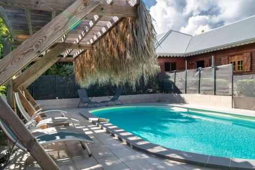 a swimming pool with chairs and a wooden pergola at Bungalow Kaz Graj in Sainte-Anne