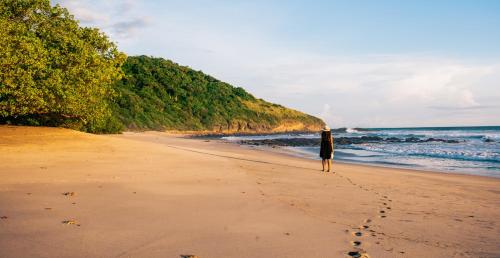 a woman standing on a beach with footprints in the sand at Punta Teonoste Beach Resort in Popoyo