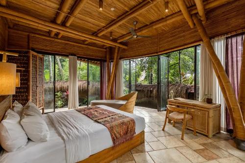 a bedroom with a bed and a desk and windows at Cacao House 4bds Eco Bamboo House, pool, near Green School Bali in Bringkit