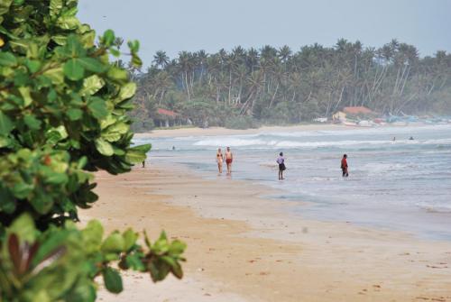 a group of people walking on the beach at ilamparuma Hotel in Weligama