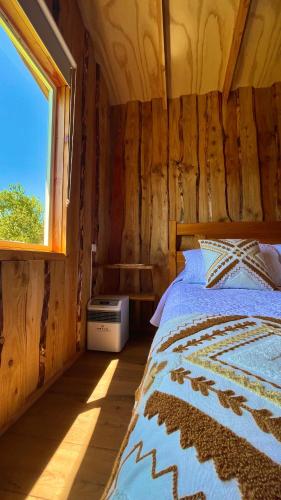 a bed in a wooden room with a window at Cabaña Estero Mágico in Cochamó