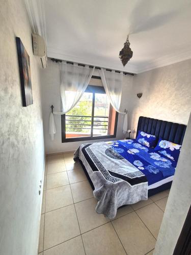 a bedroom with a bed with a blue comforter and a window at Appartement 6 personnes piscine hivernage Marrakech in Marrakesh