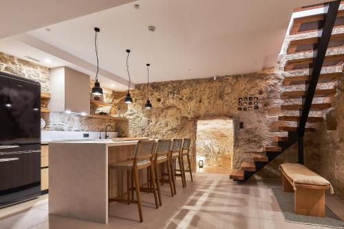 a kitchen with a bar with chairs and a stone wall at Secret Cave Villa in Matala
