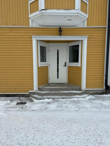 a white door on a yellow building with snow at New Central Apartment in Östhammar