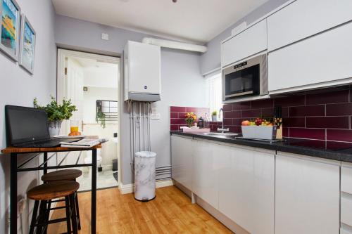 a kitchen with white cabinets and a table with a laptop at Delven House - Self Check-in, Self-Catering Serviced Apartments in Castle Donington