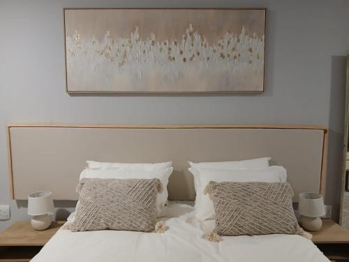a bed with white sheets and pillows under a painting at Kinn Accommodation in Bloemfontein
