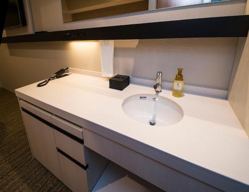 a bathroom counter with a sink and a bottle of soap at JR Inn Sapporo-eki Minami-guchi in Sapporo