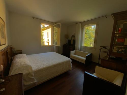 a bedroom with a bed and a chair and two windows at Palazzo Bonfiglioli in San Giovanni in Persiceto