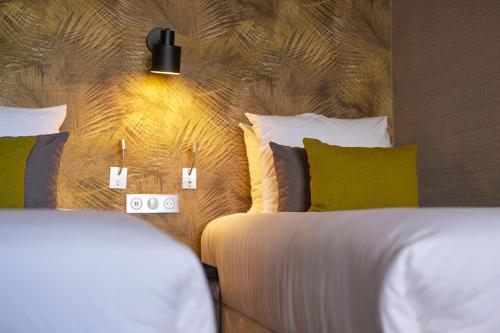a bedroom with two beds with white sheets and green pillows at Van der Valk Hotel Saint-Aygulf in Saint-Aygulf