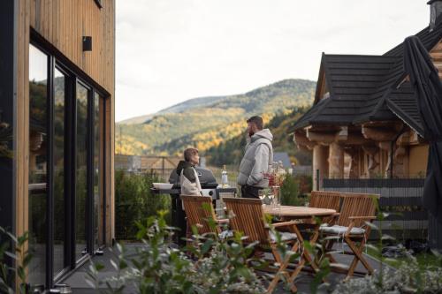 two people standing on a patio with a table and chairs at Babia Rest - całoroczny domek z balią z jacuzzi in Zawoja