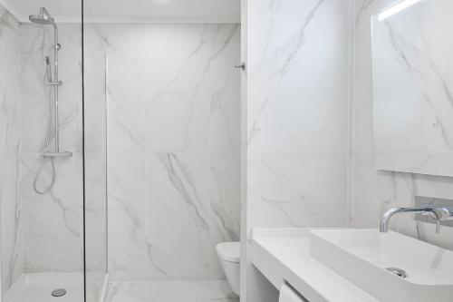 a white bathroom with a shower and a sink at Alcazar Hotel & SPA in Monte Gordo