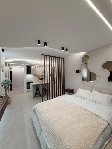 a bedroom with a large white bed and a kitchen at Mediteran Line Apartman 1 in Sombor