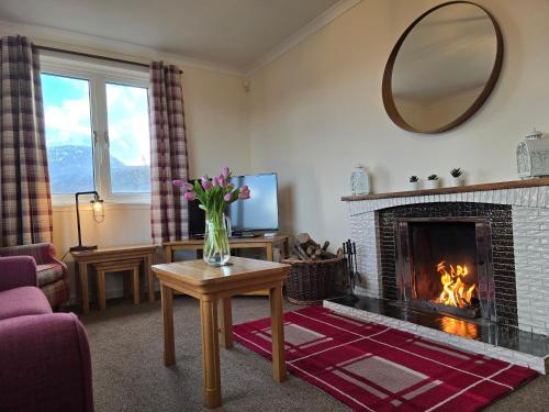 a living room with a fireplace and a vase of flowers on a table at Little Loch View in Durnamuck