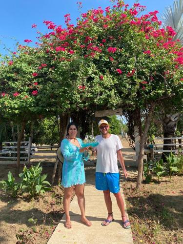 a man and woman standing in front of a tree with pink flowers at Coccoloba Beach Hotel in Dibulla
