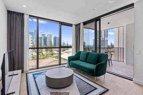 a living room with a green couch and large windows at Yves Mermaid Beach Apartments by CLLIX in Gold Coast