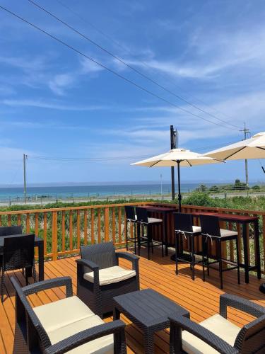 a deck with chairs and tables and umbrellas on the beach at コバルトブルービーチまで徒歩一分 貸切ヴィラ クルーズ角島 in Shimonoseki