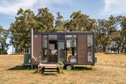 a tiny house parked in a field with a table at Tiny Divine Farmstay by Tiny Away in Korweinguboora