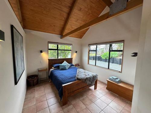 a bedroom with a bed with a blue comforter and two windows at Matapouri Sanctuary Apartment in Matapouri